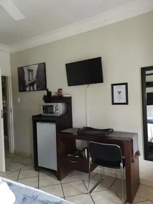 a room with a desk with a microwave and a television at Klyne Jiweel Guesthouse in Pretoria