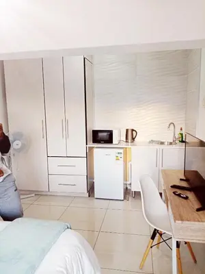 a small kitchen with white cabinets and a table and a desk at Langa's Gabedi Goshen in Pretoria