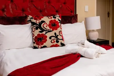 a bed with red and white pillows and a red blanket at TDM's Boutique Guest House in Pretoria