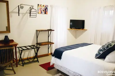 a bedroom with a bed and a television and a desk at Bosveldrus Gastehuis in Vaalwater