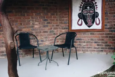two chairs and a picture of a mask on a brick wall at Bosveldrus Gastehuis in Vaalwater