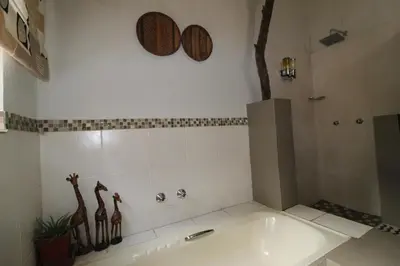 a bathroom with a tub and a shower with giraffes on the wall at Kiburi Lodge @ Kruger, a secluded Bushveld getaway in Marloth Park