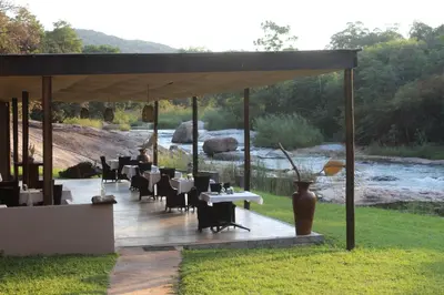 a pavilion with tables and chairs and a river at Lions Rock Rapids - Lodge in Hazyview