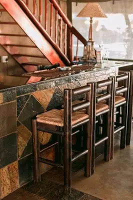 a bar with four stools at a counter with stairs at Tshukudiba Game Lodge in Tom Burke
