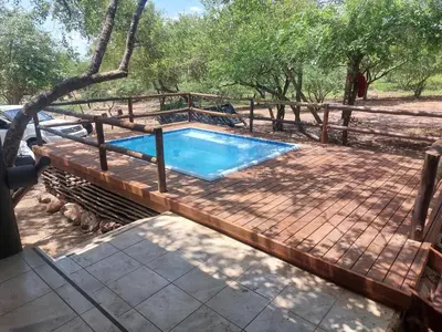 a swimming pool on a deck with a fence and trees at Coga Cottage - Marloth Park in Marloth Park