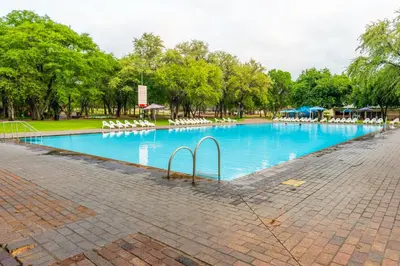 a large swimming pool with white chairs in a park at ATKV Eiland Spa in Letsitele