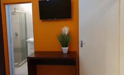 a bathroom with a television on the wall and a table with a plant at Tertius Lodge And House in Nelspruit