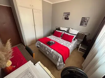 a small bedroom with a bed with red pillows at Bottie's Rock in Pretoria