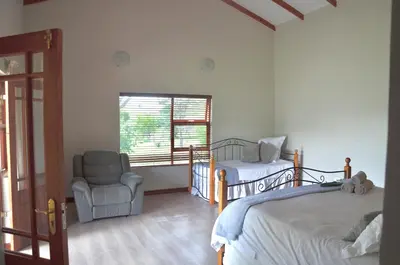 a bedroom with two beds and a chair and a window at Muqurati Lodge - Dinokeng Game Reserve in Klipdrift