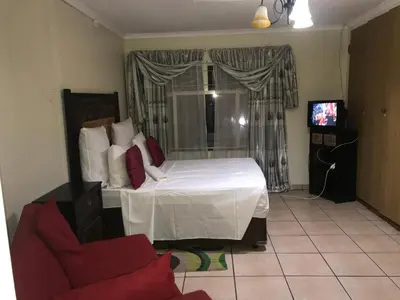 a bedroom with a bed and a chair and a television at Kaste Guesthouse Secunda in Secunda