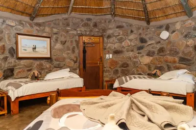 a room with two beds and a stone wall at Shumba Safari Bush Camp in Hoedspruit