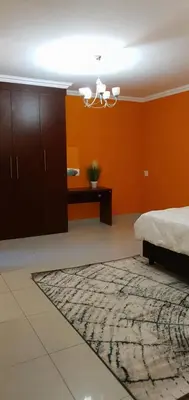 a bedroom with orange walls and a bed and a rug at TERTIUS LODGE in Nelspruit