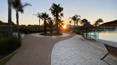 a walkway next to a swimming pool with palm trees at The Blyde - Unit 1136 in Pretoria