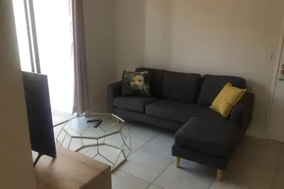 a living room with a black couch and a glass table at THE BLYDE CRYSTAL LAGOON BEACH PRETORIA in Pretoria
