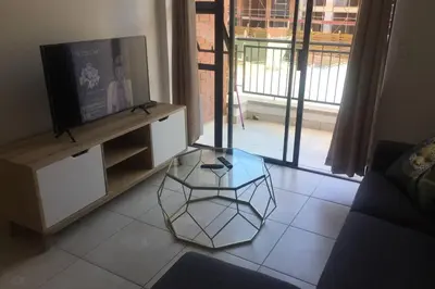 a living room with a tv and a glass table at THE BLYDE CRYSTAL LAGOON BEACH PRETORIA in Pretoria
