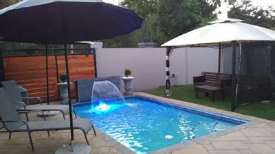 a swimming pool with an umbrella and chairs and a table at The Royal Prime Guest Lodge in Centurion