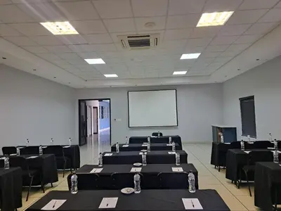 a room with rows of tables and a white screen at Oasis Hotel in Mokopane