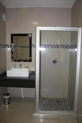 a bathroom with a shower with a sink and a mirror at Oasis Hotel in Mokopane