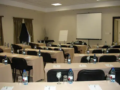 a conference room with tables and chairs and a white screen at Oasis Hotel in Mokopane