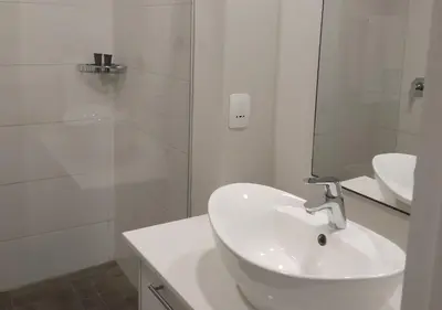 a white bathroom with a sink and a shower at Regency Apartment in Pretoria