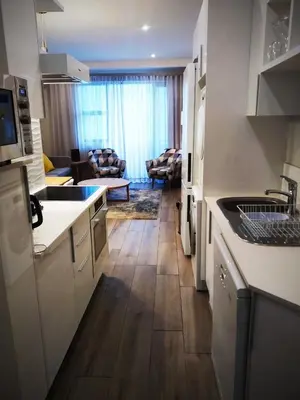 a kitchen with white cabinets and a living room at Regency Apartment in Pretoria