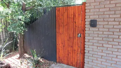 a black fence with a wooden gate next to a house at Beni Apartment in Pretoria