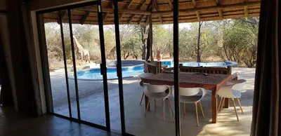 a dining room with a table and chairs and a pool at Pata Pata House in Marloth Park