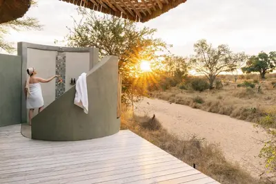 a woman is standing in a shower on a deck at Simbavati Camp George in Klaserie Private Nature Reserve