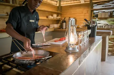 a man cooking food in a pan in a kitchen at Bundox Explorer Camp in Hoedspruit