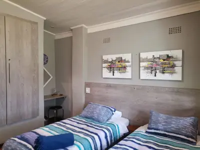 a bedroom with two beds and paintings on the wall at Karee Laagte in Leeuwfontein