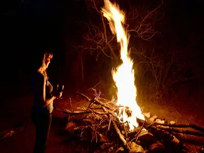a woman standing next to a fire at night at Luxury Treetop Lodge in Marloth Park