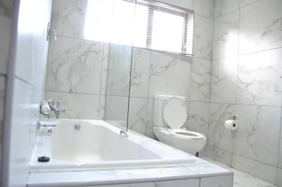 a white bathroom with a tub and a toilet at Hush Guest House in Northam