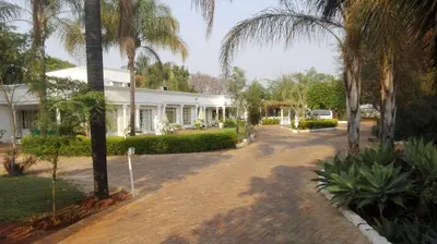a white house with palm trees and a driveway at Heatherdale Guesthouse & Shuttle Services in Pretoria