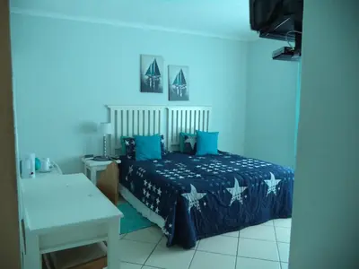 a bedroom with a bed with blue sheets and a table at Heatherdale Guesthouse & Shuttle Services in Pretoria