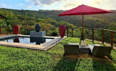 a patio with an umbrella and chairs and a pool at The Zarafa in Hazyview