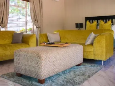 a living room with a yellow couch and a ottoman at Monacco Guest house in Erasmus