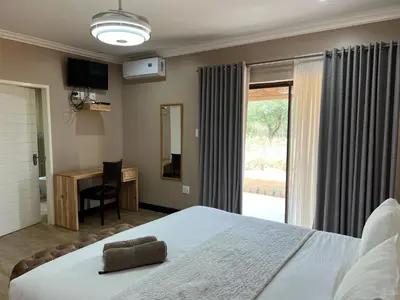 a bedroom with a bed and a desk and a window at Thabazimbi Country Lodge in Thabazimbi
