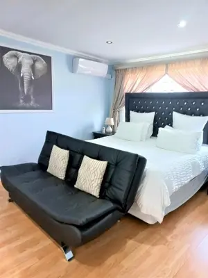 a bedroom with a large bed with a black leather couch at JB Countrylife Accommodation in Centurion