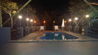 a swimming pool at night with a table and a umbrella at SVH Bush Lodge in Marloth Park