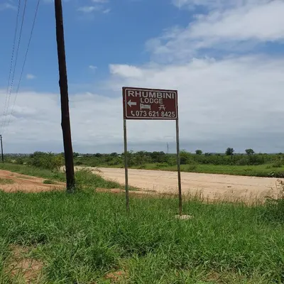 a sign in the grass next to a dirt road at Rhumbini Lodge in Malamulele