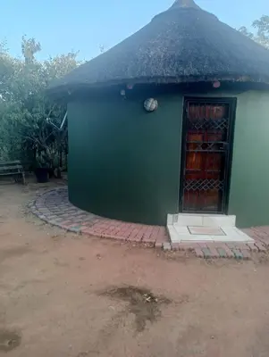 a small green building with a thatched roof at Rhumbini Lodge in Malamulele