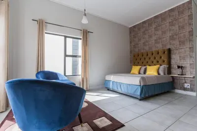 a bedroom with a bed and a blue chair at Alimama Spaces: The Manson's Green Creek Studio in Pretoria