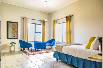 a bedroom with a bed and blue chairs and windows at Alimama Spaces: The Manson's Green Creek Studio in Pretoria
