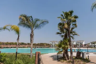 a pool with palm trees and houses in the background at #Alimama Spaces The Fountain Blyde in Pretoria