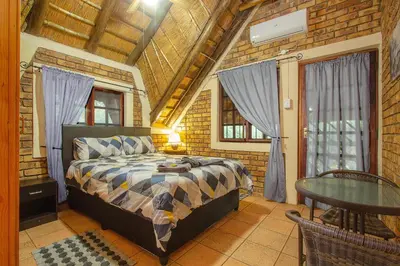 a bedroom with a bed and a table and windows at Inkwazi Place in Marloth Park