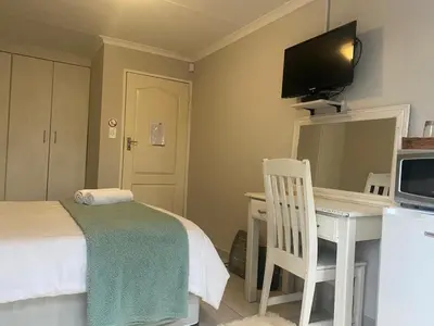 a bedroom with a bed and a desk with a television at Ndzuti Guest House in Witbank