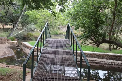 a metal bridge over a river with a walkway at Wilgeboomsdrift Safaris in Modimolle