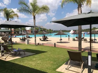 a resort with a pool and palm trees and chairs and umbrellas at The Blyde Riverwalk estate, Crystal Lagoon in Pretoria