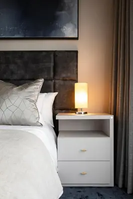 a bed with a white nightstand with a lamp on it at Menlyn Apartment - Black Marble in Pretoria