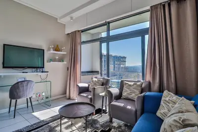 a living room with a blue couch and a large window at 301 Menlyn Maine Trilogy Apartment in Pretoria